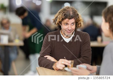 Happy middle-age man and young girl chatting over cup of coffee at table in light cafe, face of middle-age man and back of girl 135805724