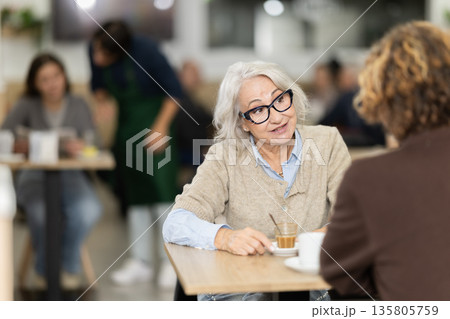 Positive grandmother in cafe sits near adult son, has nice conversation and discusses news of day Positive grandmother in cafe sits near adult son, has nice conversation and discusses news of day 135805759