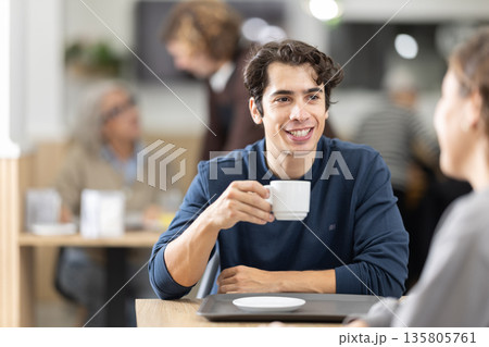 Young couple drinking coffee and chatting while sitting at table in cozy cafe Young couple drinking coffee and chatting while sitting at table in cozy cafe 135805761