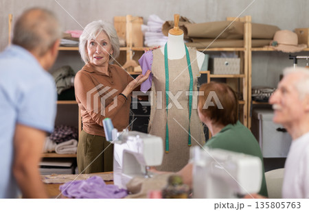 Female teacher demonstrating sleeve placement on dress form to elderly students Female teacher demonstrating sleeve placement on dress form to elderly students 135805763