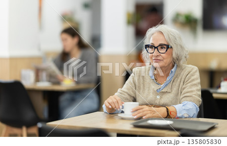 Aged european woman drinking fresh coffee at table in cafe Aged european woman drinking fresh coffee at table in cafe 135805830