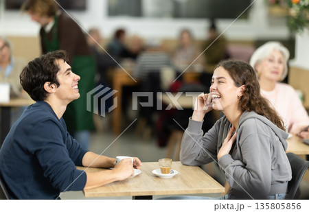 Young couple drinking coffee and chatting while sitting at table in cozy cafe 135805856