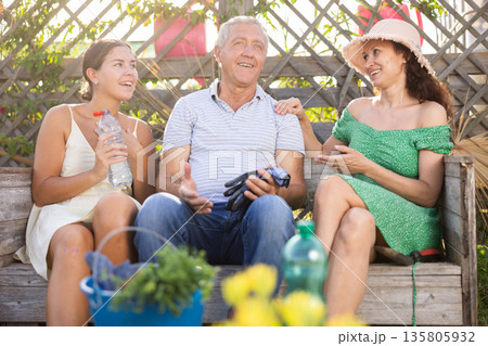 Woman in straw hat is sitting on wooden bench and chatting sweetly with sister and senior father Woman in straw hat is sitting on wooden bench and chatting sweetly with sister and senior father 135805932