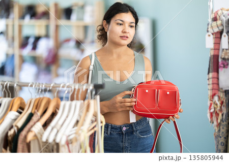 Latina woman choosing a stylish handbag in store with interest Latina woman choosing a stylish handbag in store with interest 135805944