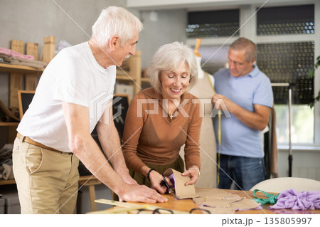 Elderly man and woman working with mannequin and making pattern in class 135805997