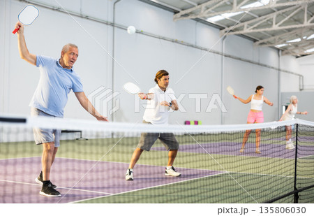 Two athletic men of different ages are playing a game of pickleball on a court inside sports facility Two athletic men of different ages are playing a game of pickleball on a court inside sports facility 135806030