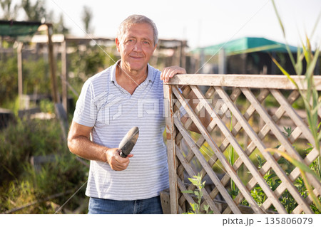 Portrait of happy elderly man with hoe in her hands in her garden Portrait of happy elderly man with hoe in her hands in her garden 135806079