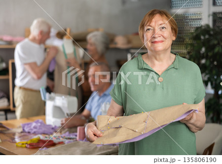 Elderly female participant present fabric billet, other people learn craft of tailor Elderly female participant present fabric billet, other people learn craft of tailor 135806190