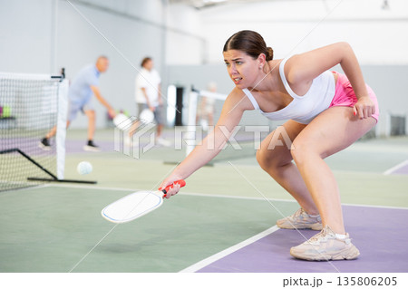 Young woman bouncing ball in pickleball game on court with racket 135806205