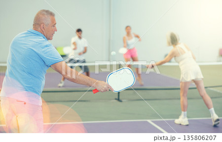 Rear view of elderly man playing pickleball on indoor court Rear view of elderly man playing pickleball on indoor court 135806207