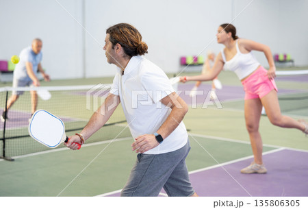 Sporty man pickleball tennis player trains on the indoor court using a racket to hit ball Sporty man pickleball tennis player trains on the indoor court using a racket to hit ball 135806305