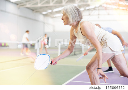 Sporty senior woman playing pickleball on indoor court Sporty senior woman playing pickleball on indoor court 135806352
