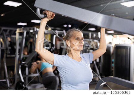 Mature female athlete working out at shoulder press machine in gym Mature female athlete working out at shoulder press machine in gym 135806365
