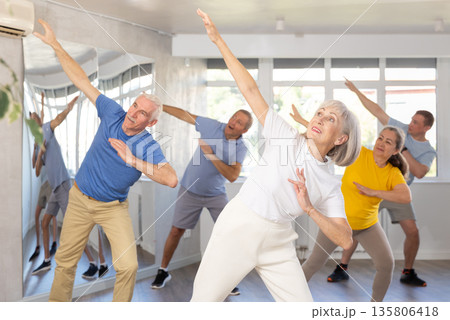 Elderly woman practicing Tai Chi with group in training room 135806418