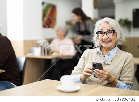 Elderly woman holding mobile phone in coffee shop Elderly woman holding mobile phone in coffee shop 135806433