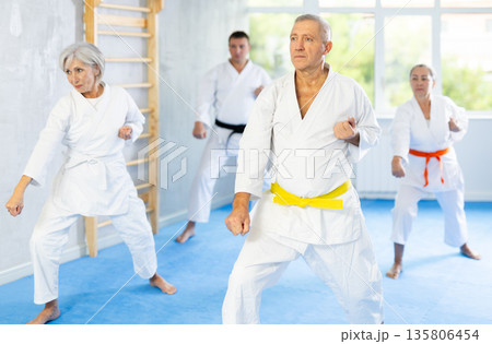 Old man attendee of karate classes practicing kata standing in row with others Old man attendee of karate classes practicing kata standing in row with others 135806454