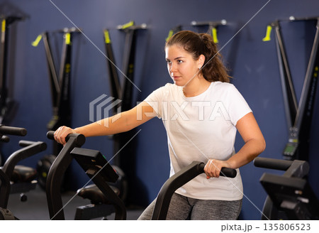 Young girl cycling on stationary bike during training in gym Young girl cycling on stationary bike during training in gym 135806523