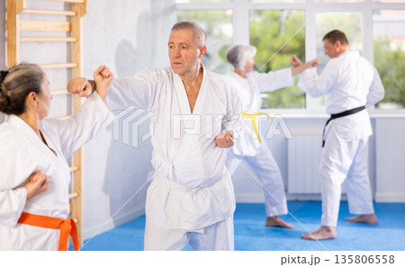 Old man attendee of karate classes fighting with his opponent in sports hall Old man attendee of karate classes fighting with his opponent in sports hall 135806558