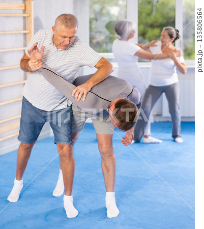 Self defense lesson - elderly man twists the arm of attacking man with painful hold in gym Self defense lesson - elderly man twists the arm of attacking man with painful hold in gym 135806564