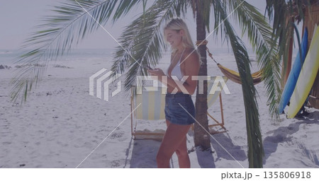 Holding smartphone woman wearing bikini top and denim shorts at beach with surfboards, copy space Holding smartphone woman wearing bikini top and denim shorts at beach with surfboards, copy space 135806918