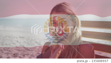Relaxing woman wearing red bikini sitting on wooden lounge chair at beach, with emblem flag overlay 135806937