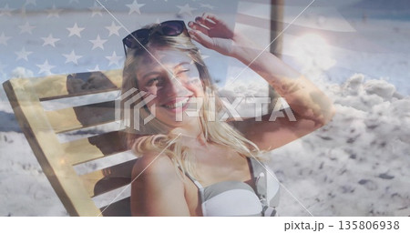 Reclining woman in bikini adjusting sunglasses on lounge chair at beach, with American flag overlay Reclining woman in bikini adjusting sunglasses on lounge chair at beach, with American flag overlay 135806938