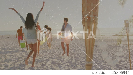 Waving beachgoer wearing white shorts greeting friends on sandy beach with surfboard and lanterns 135806944