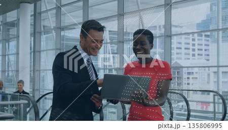 Discussing suited man and woman in red top examining laptop at office lobby, with glass panels 135806995