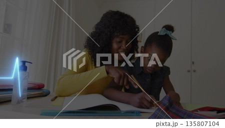 Leaning mother in yellow top pointing at workbook while daughter writing at study nook, with pencil 135807104