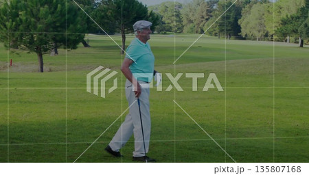 Walking senior golfer in green polo and white trousers across fairway, with golf club and glove 135807168