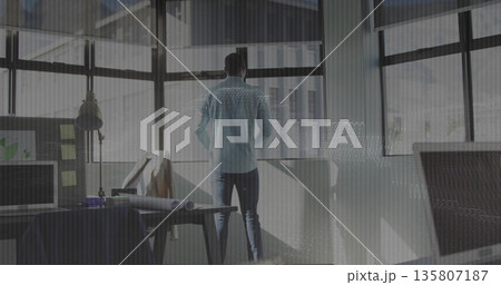 Standing architect wearing shirt and trousers gazing through windows in office, with monitor 135807187
