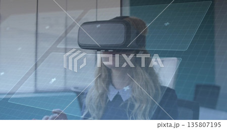 Navigating professional wearing blazer using VR headset at desk, with floating UI panels 135807195