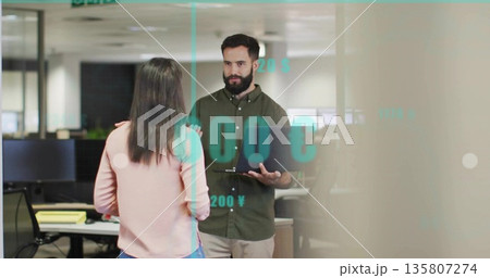 Discussing financial data professional holding laptop in office floor with currency symbols overlay Discussing financial data professional holding laptop in office floor with currency symbols overlay 135807274
