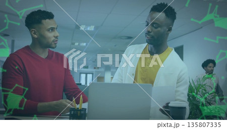 Standing two coworkers holding paper document and using laptop at office desk with coffee cup Standing two coworkers holding paper document and using laptop at office desk with coffee cup 135807335