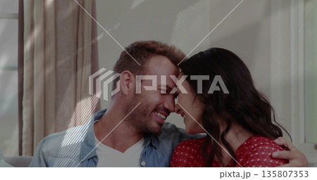 Smiling couple leaning with foreheads touching on sofa in living room, with curtains, window frame 135807353