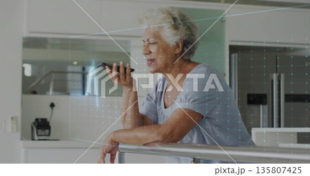 Leaning senior woman holding smartphone projecting holographic grid in kitchen, with metal railing Leaning senior woman holding smartphone projecting holographic grid in kitchen, with metal railing 135807425