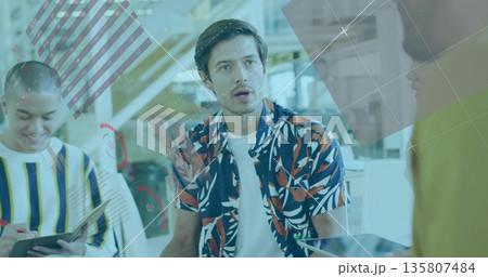 Speaking male worker wearing patterned shirt in modern workspace, with tablet laptop monitors Speaking male worker wearing patterned shirt in modern workspace, with tablet laptop monitors 135807484
