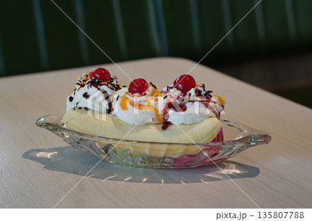 side view three flavors of ice cream, decorated with whipped cream and cherries and top with orange jam or strawberry jam and slice banana split, served in a boat-shaped glass on wooden floor , green side view three flavors of ice cream, decorated with whipped cream and cherries and top with orange jam or strawberry jam and slice banana split, served in a boat-shaped glass on wooden floor , green 135807788