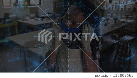 Woman demonstrating augmented reality while wearing VR headset and apron at makerspace, workbenches 135808563