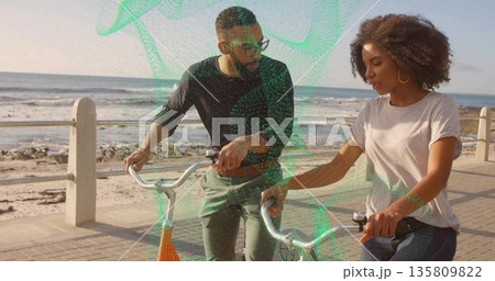 Walking side by side, friends holding bicycles on seaside promenade by railing and posts, chatting Walking side by side, friends holding bicycles on seaside promenade by railing and posts, chatting 135809822