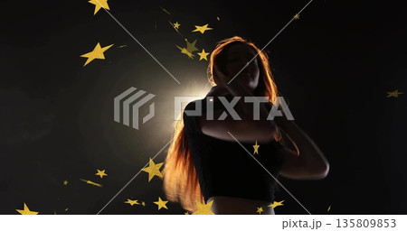 Woman being backlit and wearing crop-top in studio, featuring gold star confetti on dark backdrop Woman being backlit and wearing crop-top in studio, featuring gold star confetti on dark backdrop 135809853