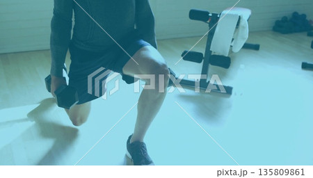 Performing weighted lunge man in athletic shirt and shorts by home gym bench with hex dumbbells Performing weighted lunge man in athletic shirt and shorts by home gym bench with hex dumbbells 135809861