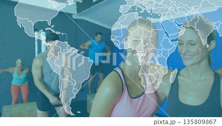 Two women in sportswear jumping onto wooden plyometric boxes in gym studio, with metal pull-up rig 135809867