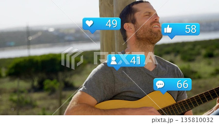 Strumming musician in gray tee by wooden post at shore, with acoustic guitar and floating icons 135810032