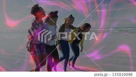 Walking four friends linking arms and leaning in along sandy shoreline, magenta-pink glow Walking four friends linking arms and leaning in along sandy shoreline, magenta-pink glow 135810096