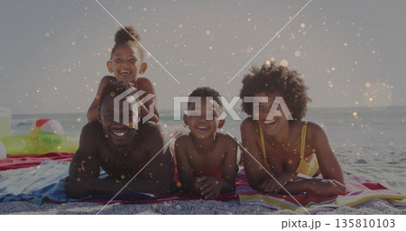 Lying family in swimwear smiling on striped towels at shoreline, with swim ring and beach ball Lying family in swimwear smiling on striped towels at shoreline, with swim ring and beach ball 135810103