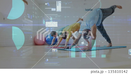 Holding downward dog pose partners practicing yoga in fitness studio, with mats, balls, data charts Holding downward dog pose partners practicing yoga in fitness studio, with mats, balls, data charts 135810142