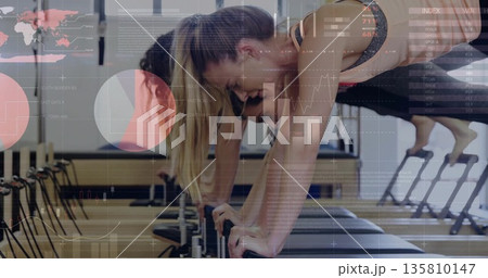 Holding planks, five women exercising on reformer machines in wood floor studio with mirrored wall Holding planks, five women exercising on reformer machines in wood floor studio with mirrored wall 135810147