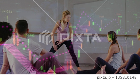 Instructor guiding participants through wide legged pose in studio, with financial chart overlays Instructor guiding participants through wide legged pose in studio, with financial chart overlays 135810148