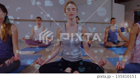 Meditating central woman and fellow yoga participants on mats in studio, with digital overlay icons Meditating central woman and fellow yoga participants on mats in studio, with digital overlay icons 135810151